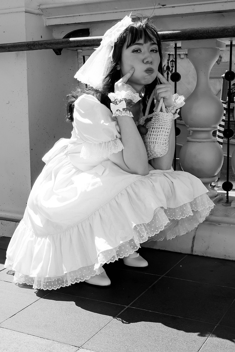 Black-and-white street portrait in a white ruffled dress
